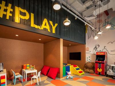 Barevná dětská herna s hračkami, sezením a arkádovým herním automatem.