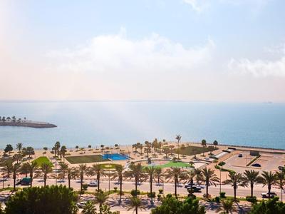 Pohled na hotelový bazén a palmy u moře za jasné oblohy.