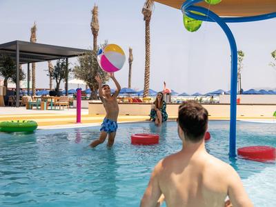 Menschen spielen mit Ball im Pool bei sonnigem Wetter in einem Resort.