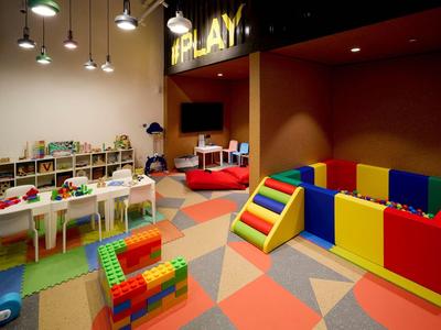 Kinder-Spielzimmer mit buntem Spielbereich, Tischen, Stühlen und Spielzeugregalen.