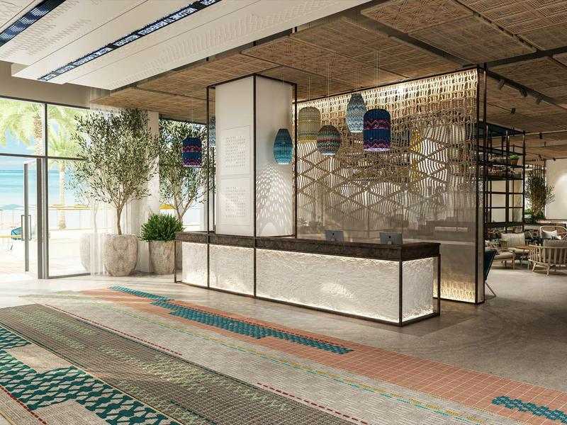 Světlá hotelová lobby s moderní recepcí, velkými okny a dekorativními koberci.