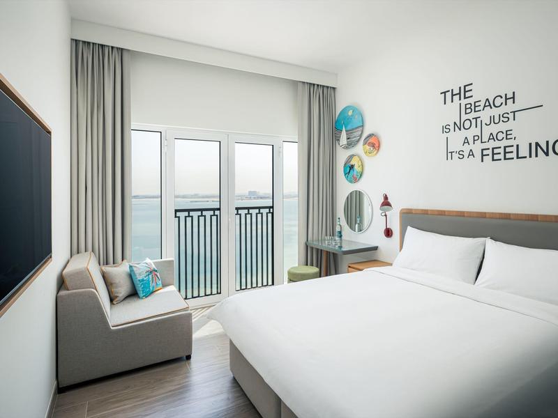 Moderní hotelový pokoj s výhledem na moře, dvojlůžkem, pohovkou a dekorativními nástěnnými prvky.