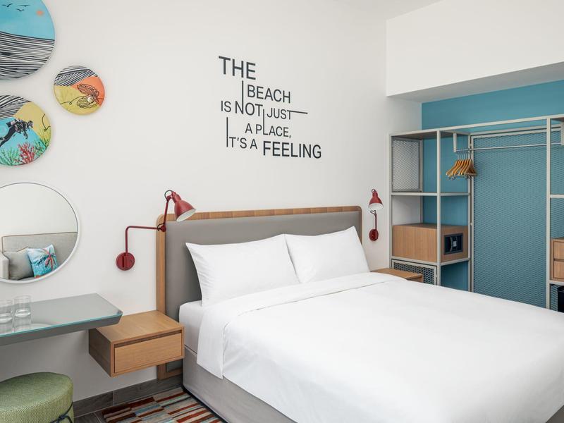 Moderní hotelový pokoj s manželskou postelí, nástěnnými policemi, zrcadlem a dekorací s nápisem na zdi.