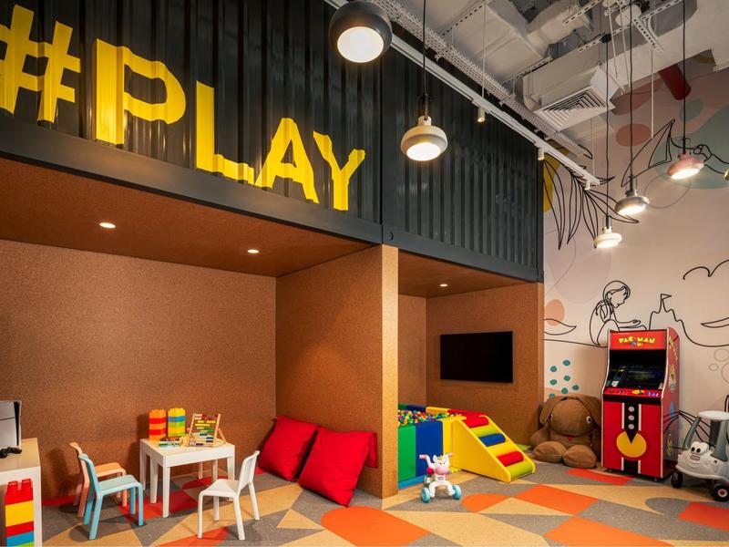 Barevná dětská herna s hračkami, sezením a arkádovým herním automatem.