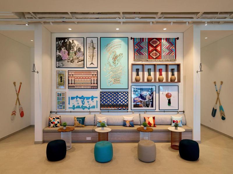 Moderní hotelový salonek s barevnými polštáři a námořnickými obrazy na zdi.