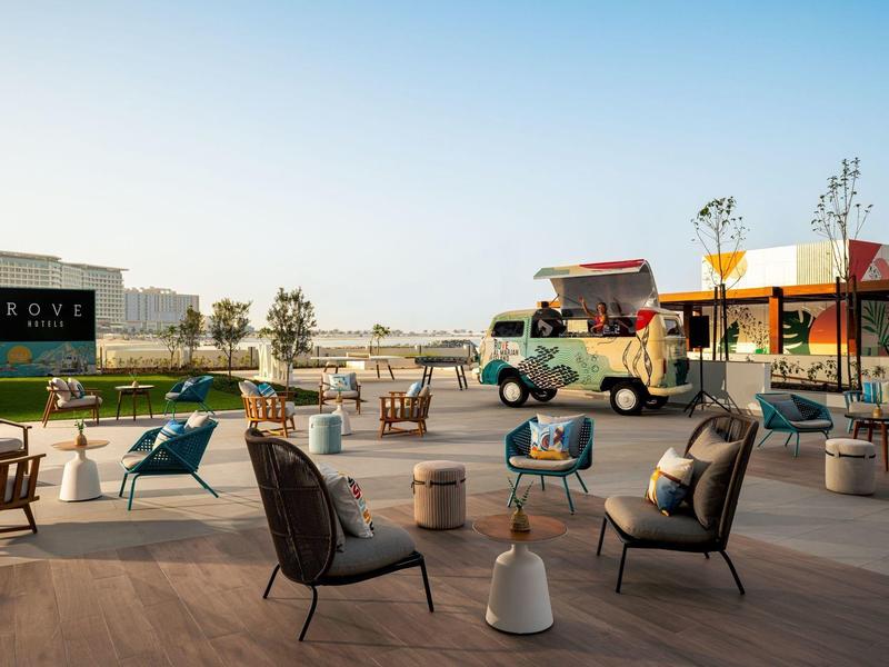 Moderní venkovní lounge s židlemi a stoly na dřevěné terase za denního světla.