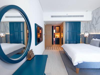Modern eingerichtetes Hotelzimmer mit Bett, Spiegel und blauen Akzenten.