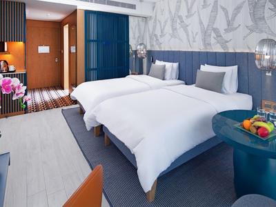 Modernes Hotelzimmer mit zwei Betten, blau-grauen Wänden und einem runden Tisch mit Obst.