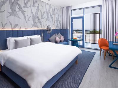 Modernes Hotelzimmer mit großem Bett, Blautönen und Balkon mit Aussicht.