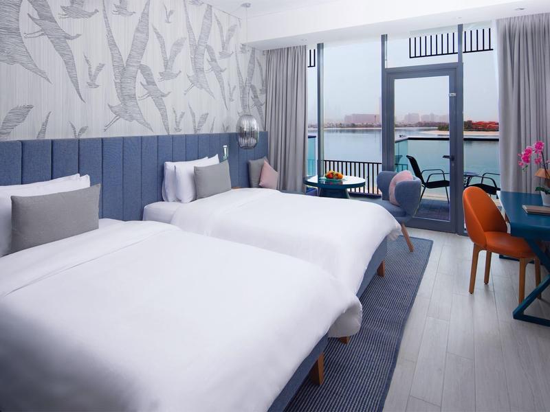 Modernes Hotelzimmer mit zwei Einzelbetten, Schreibtisch und Meerblick durch große Fenster.