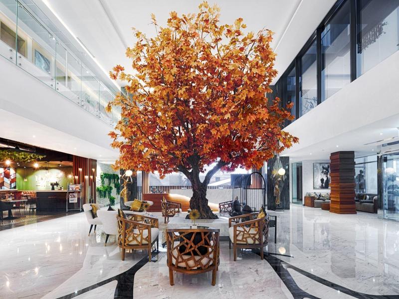 Ein großer herbstlich-brauner Baum steht mittig in einem modernen Einkaufszentrum mit glänzendem Boden.