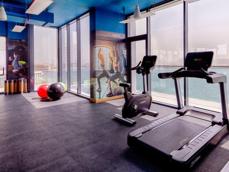 Moderner Fitnessraum mit Laufbändern, Ergometer, bunten Gymnastikbällen und großen Fenstern.