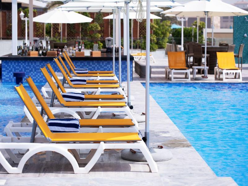 Reihe gelber Liegestühle mit blauen Kissen neben einem großen blauen Pool unter weißen Sonnenschirmen.