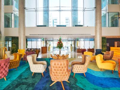 Moderner, heller Lobbybereich mit farbenfrohen Sesseln und einem Blumenarrangement auf einem Tisch.