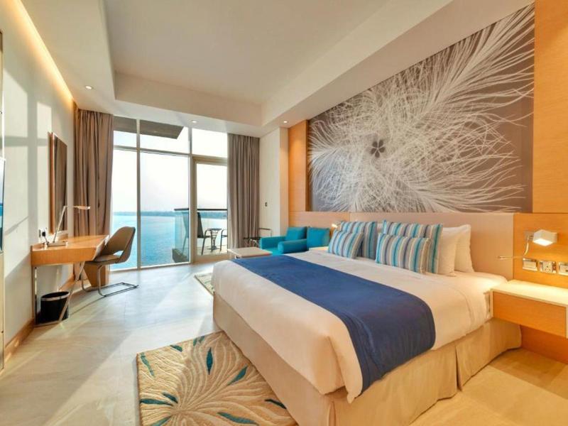 Modernes Hotelzimmer mit großem Bett, Schreibtisch und Balkon mit Meerblick.