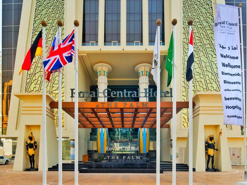 Eingang eines Hotels mit fünf Fahnen vor Gebäudefassade in hellem Gelb und Grün.