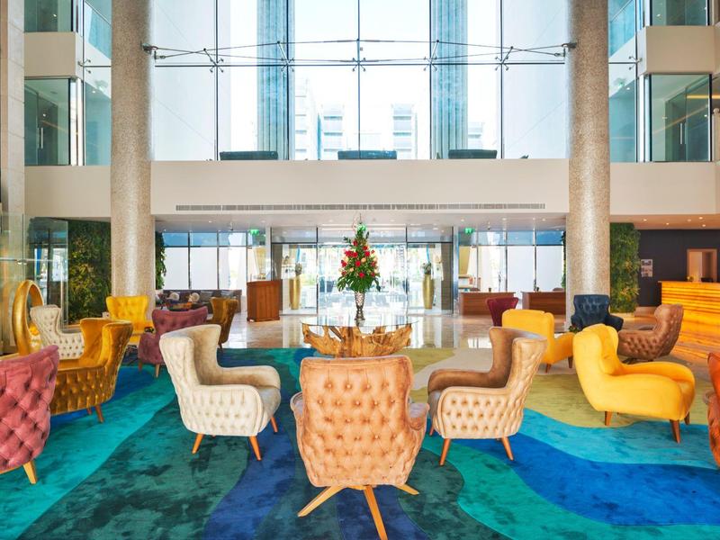Moderner, heller Lobbybereich mit farbenfrohen Sesseln und einem Blumenarrangement auf einem Tisch.