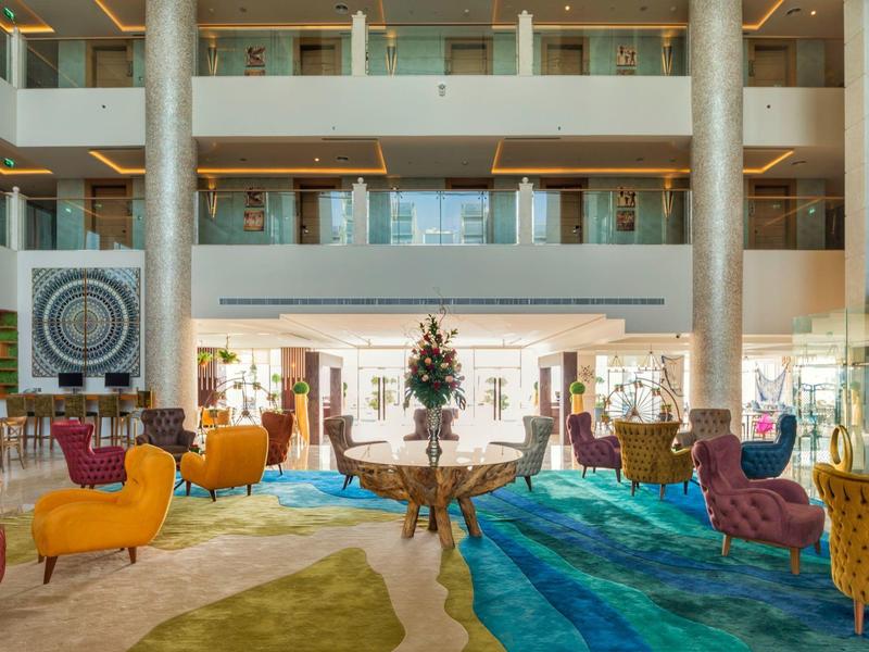 Großer heller Hotellobby mit bunten Sesseln, Glasgeländern und dekorativem Mittelstück.