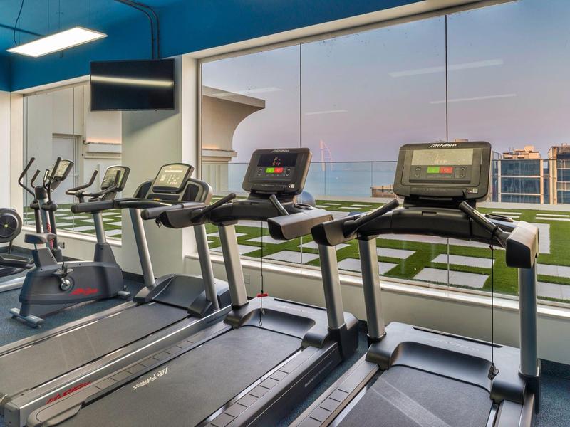 Helles Fitnessstudio mit Laufbändern und Fahrrädern, großen Fenstern und Blick auf Wasser und Hafen.