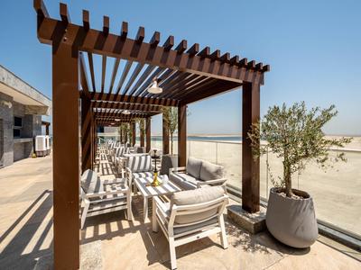 Terraza con pérgola de madera, sillas blancas y mesa, junto a una planta en maceta grande