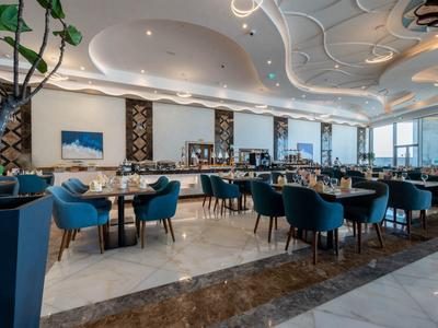 Restaurante elegante con sillas azules modernas, mesas blancas y grandes ventanales con vistas a la ciudad.