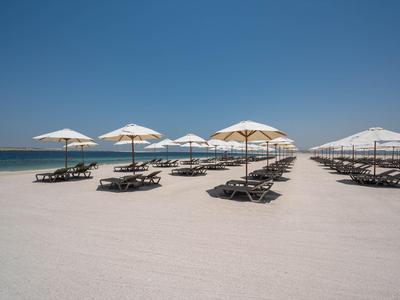 Strand met witte parasols en ligstoelen onder een heldere blauwe lucht.