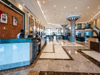 Amplio vestíbulo de hotel con recepción, suelo de mármol y iluminación moderna.