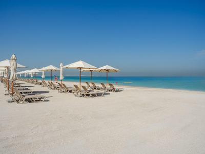 Playa vacía con tumbonas y sombrillas bajo cielo despejado junto al mar.