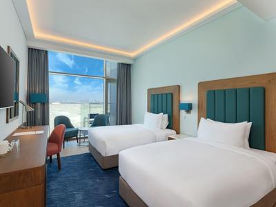 Habitación de hotel moderna con dos camas dobles, ventana grande y vista al mar.