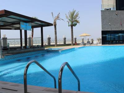 Piscina exterior moderna con escalera, sombrilla y palmeras en un hotel junto al mar.