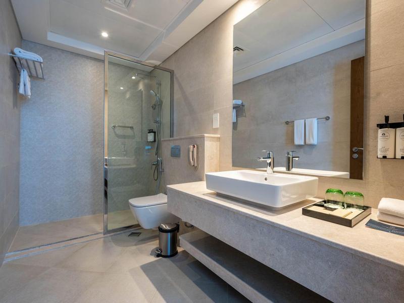 Moderna habitación de hotel con lavabo grande, ducha de vidrio y toallas ordenadas