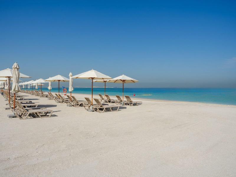 Playa vacía con tumbonas y sombrillas bajo cielo despejado junto al mar.