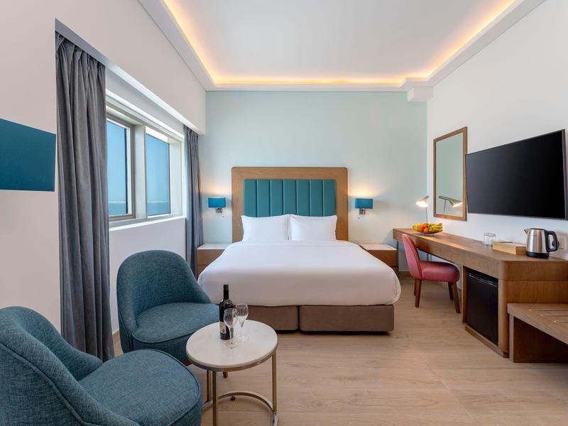 Habitación de hotel moderna con cama grande, área de estar, escritorio y ventana grande.