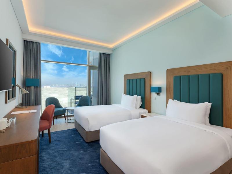 Habitación de hotel moderna con dos camas dobles, ventana grande y vista al mar.