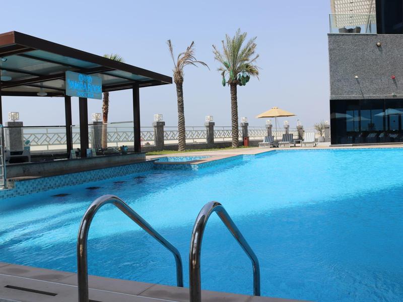 Piscina exterior moderna con escalera, sombrilla y palmeras en un hotel junto al mar.