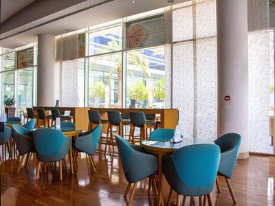 Nowoczesna jadalnia z niebieskimi krzesłami, drewnianymi stołami i dużymi oknami z widokiem na zewnątrz.