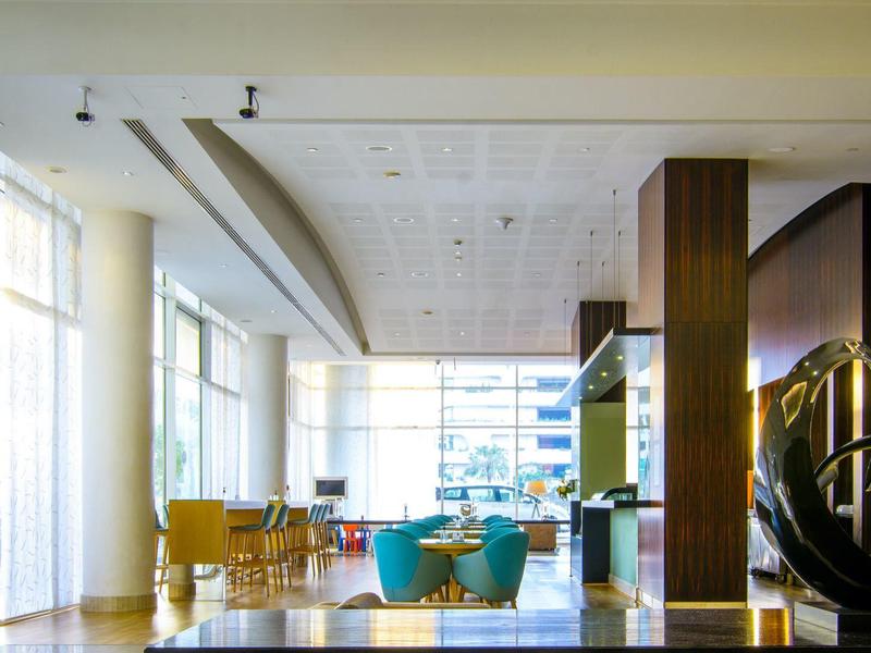 Bright hotel lobby with large windows, modern furnishings, and art sculptures.