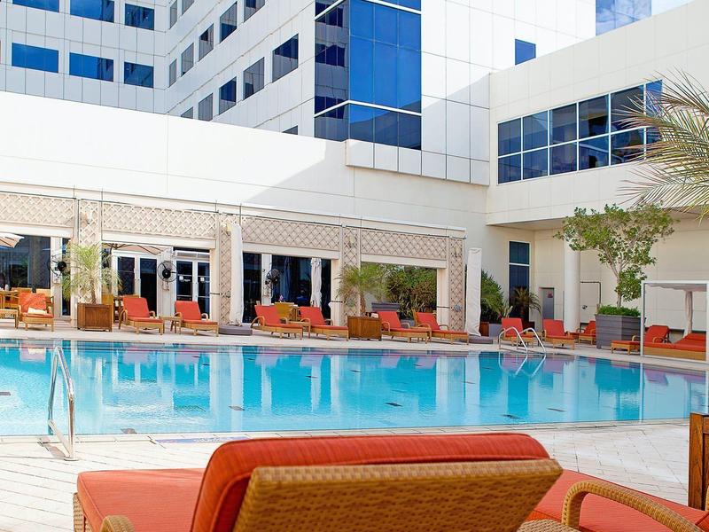 Hotel pool with orange lounge chairs and a white multi-story building in the background