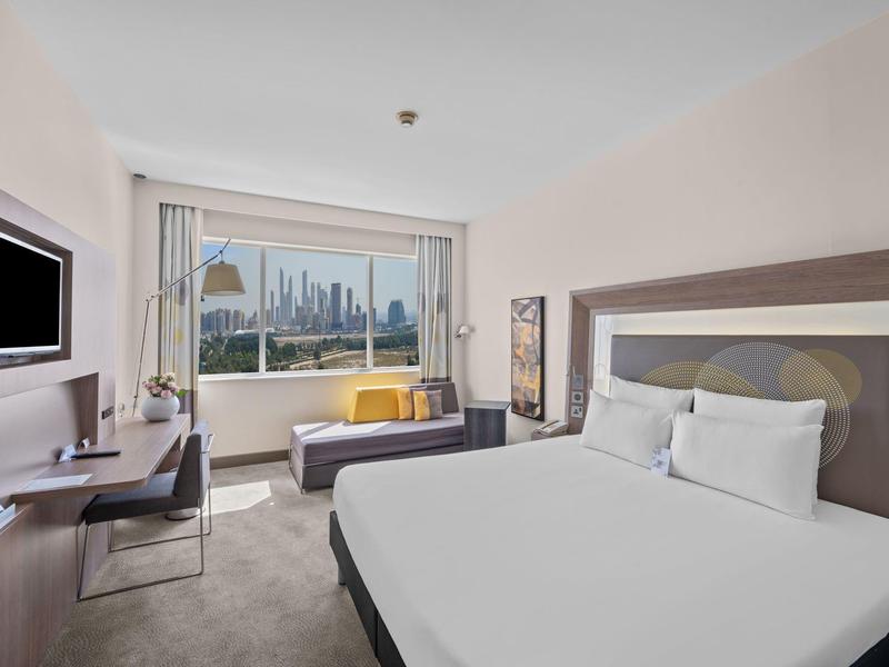 Modern hotel room with large bed, desk, and city view through the window.