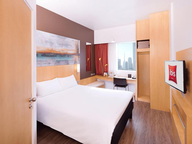 Modern hotel room with large bed, desk, city view, and wall-mounted TV.