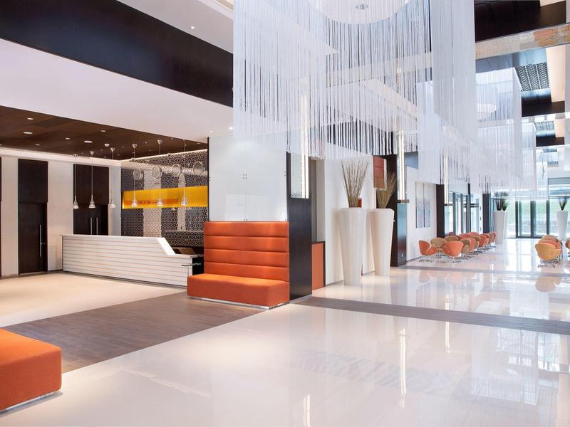 Bright, modern hotel lobby with white floors, orange seats, and elegant chandelier.