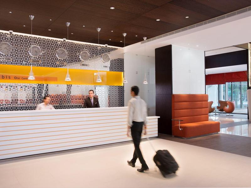 Modern hotel lobby with reception desk, guests, and various seating areas.