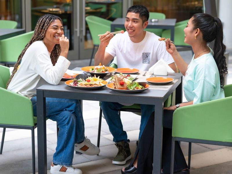 Three young adults dining together at a table in a modern restaurant.