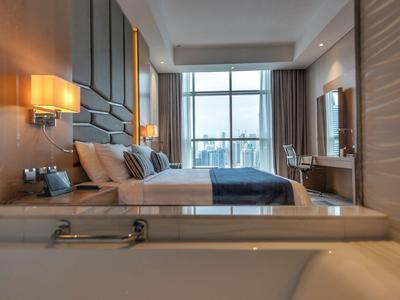 Modern hotel room with large bed, bathtub, and big window with city view.