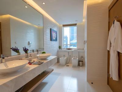 Modern hotel bathroom with double sinks, large mirror, window with city view, and white bathrobes.