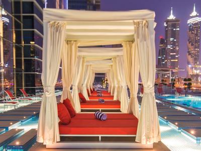 Luxury pool lounges with white curtains and red cushions at night in the city.