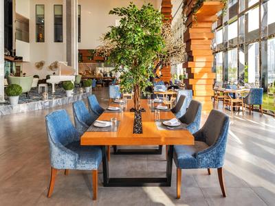 Area ristorante luminosa con tavolo in legno, sedie blu e grandi finestre che lasciano entrare la luce naturale.