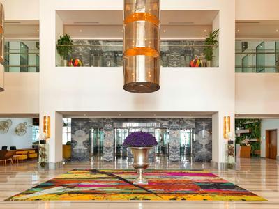 Bright hotel lobby with large colorful rug and central flower arrangement.
