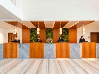 Modern hotel lobby with wooden and marble reception desk, illuminated by hanging lamps.