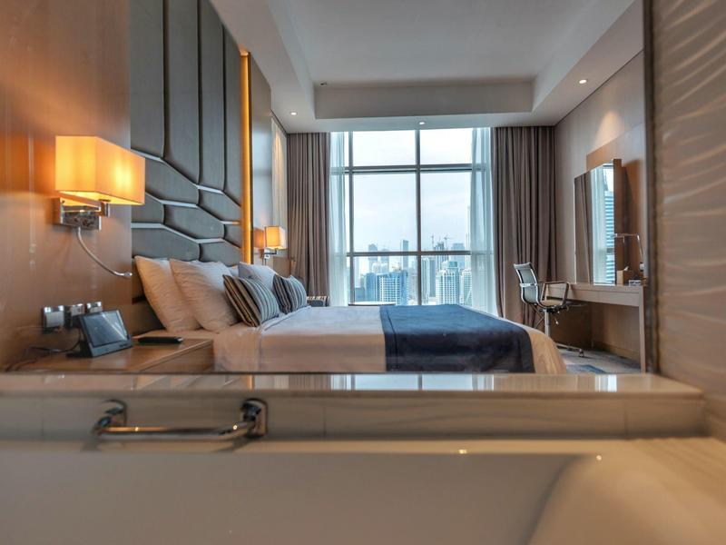 Modern hotel room with large bed, bathtub, and big window with city view.